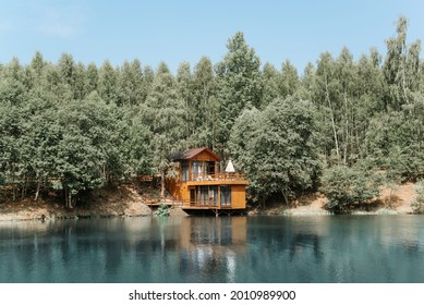 Modern Aesthetic Wooden House On The Lake. Exterior Of A Country House, Cottage On The Water Near The Forest, Summer Day.