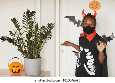 Modern African American boy wearing devil costume with red horns and black mask on face saying bye to his parents and going to trick or treat with friends.. - Powered by Shutterstock