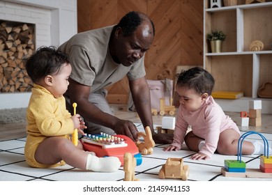 Modern African American Father Sitting On Floor In Living Room At Home Playing With His Lovely Twin Babies