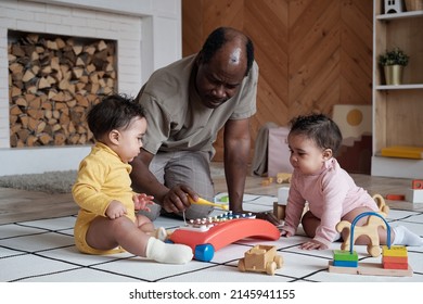 Modern African American Man Spending Time At Home With His Twin Babies Showing Them How To Play Toy Xylophone