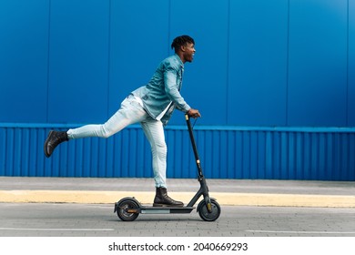 modern african american on electric scooter, business man is one to work, student is one to study, against the background of a blue building, side view
