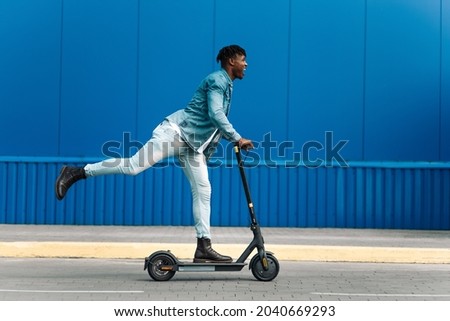 modern african american on electric scooter, business man is one to work, student is one to study, against the background of a blue building, side view