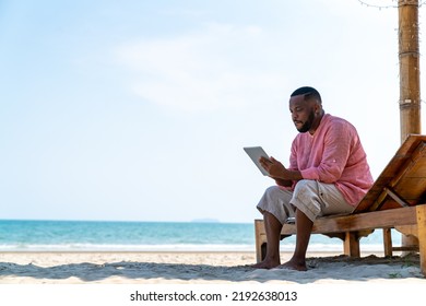 Modern African businessman working on digital tablet for business stocks trading on tropical beach in summer sunny day. Freelancer guy enjoy outdoor lifestyle work and travel on summer travel vacation - Powered by Shutterstock