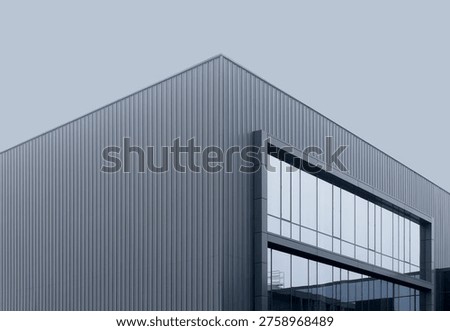Modern angular building with metal facade and glass window corner detail. Minimal structure shows sharp geometry and clean composition. Concept of contemporary architecture design exterior.