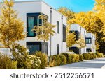 Modern Apartment Building Exterior with White Facade and Trees in Autumn Germany. Contemporary Residential Multifmily Low rise Buildings Townhouse in Autumn Landscaping.