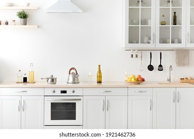 Modern apartment for sale and rent real estate, simply, scandinavian, minimalist interior. Kettle and utensils on white furniture, shelves with dishes and potted plant in daylight, empty space