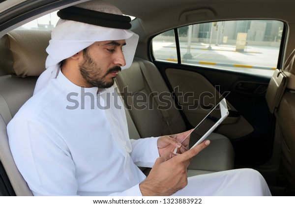 Modern Arabic business man using smart tablet\
device while inside a\
vehicle