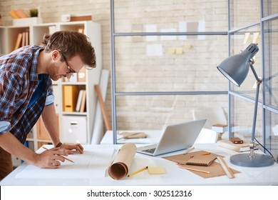 Modern architect looking at blueprint with sketch of construction in office
