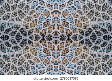 a modern architectural facade featuring a complex, geometric pattern of white, hexagonal and irregularly-shaped frames. The frames enclose various glass panels, creating a mosaic-like effect.