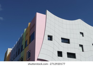 Modern architectural facade featuring white curved design with vibrant rainbow colors and geometric windows against a blue sky