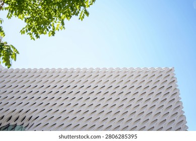 Modern architectural facade with geometric patterns under a clear blue sky and green foliage.