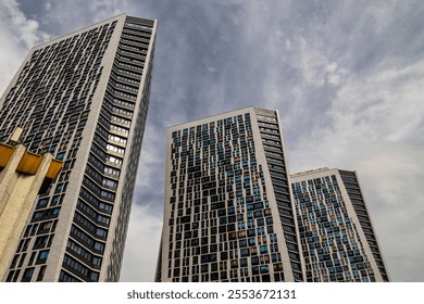 A modern architectural shot featuring three high-rise buildings with a geometric facade of glass windows under a partly cloudy sky, showcasing urban design and contemporary style. - Powered by Shutterstock