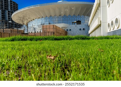 A modern architectural structure with a curved facade and glass elements, set against a vibrant green lawn. The scene highlights the contrast between the natural greenery and the futuristic design - Powered by Shutterstock