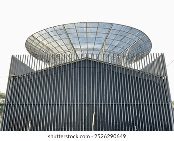 A modern architectural structure featuring vertical metal bars surrounding a sleek black building, topped with a unique circular, glass like canopy