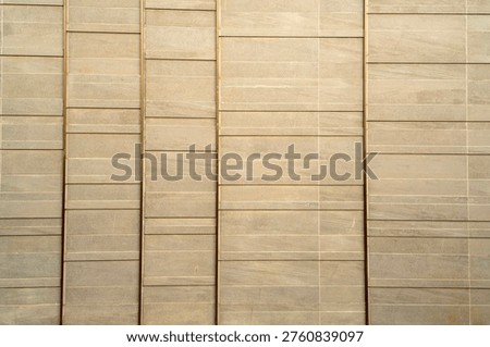 Modern architectural wall featuring textured beige stone tiles separated by vertical bronze metallic strips. Clean linear design for luxury building exterior or minimalist interior background.