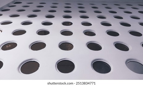 A modern architectural wall with numerous circular windows arranged in a geometric pattern, viewed from below. - Powered by Shutterstock