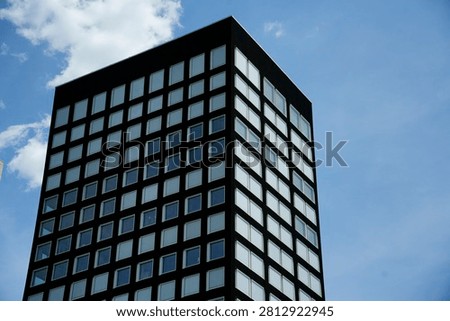 Modern architecture featuring a black building facade with many repeating square windows facing a blue sky