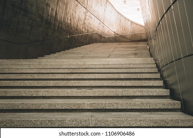 a modern architecture loft concept design of concrete stair with granite surface texture at the walking entrance of a modern exhibition hall building with a sun light at the end of the tunnel.