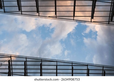 Modern architecture: a low-angle view of a glass ceiling or facade with a metal structure against a cloudy sky with sunset hues.