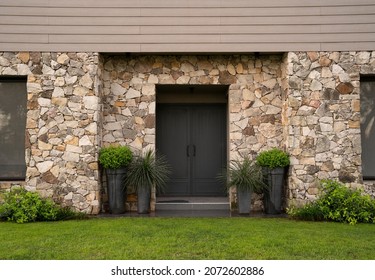 Modern architecture. Residential facade design. Closeup view of new house iron front door, stonewall and decorative plants Buxus sempervirens, also known as boxwood bush, growing in pots. - Shutterstock ID 2072602886