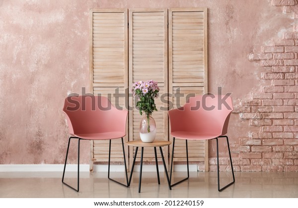Modern armchairs and bouquet of flowers on table\
near color wall