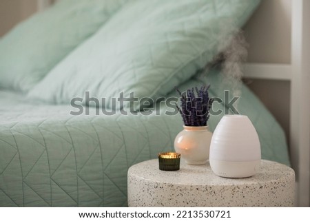 Modern aroma oil diffuser or humidifier on the table whith lavender flowers and a candle near the bed. Aromatherapy and relaxing.