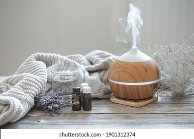 Modern aroma oil diffuser on wood surface with knitted element, water and oils in jars.