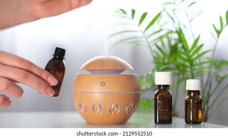 Modern aroma oil diffuser on the white table. Spa concept for body and health care. female is adding essential oil to an aroma diffuser.
