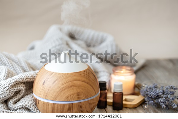 Modern aroma oil\
diffuser on wood surface with knitted element, candle and lavender\
oil on a blurred\
background.