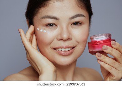 Modern Asian Female With Facial Cream Jar And Eye Cream On Face Isolated On Blue Background.