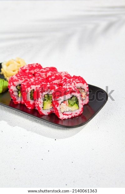 Modern asian food - alaska maki sushi on black\
plate on white concrete background. Sushi roll with crab, avocado,\
cucumber inside and tobiko caviar outside. Maki sushi with masago\
caviar
