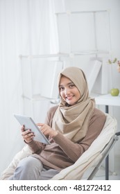 modern asian woman wearing hijab using tablet pc while sitting in a living room