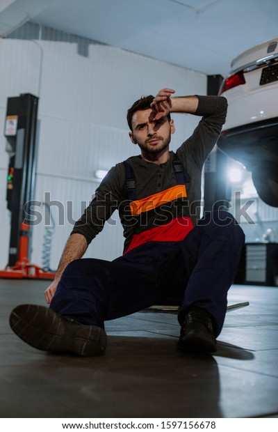 In a modern auto service\
center closeup to the camera mechanic man charismatic showing very\
tired