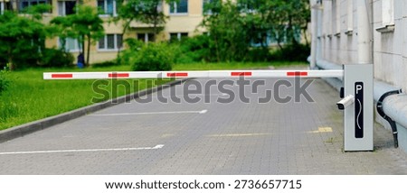 Modern automatic parking barrier with security camera and white boom arm with red stripes guarding entrance to private residential parking lot in the city. Closed gate, boom barrier blocking access