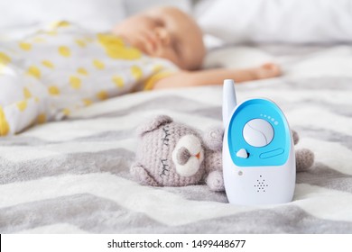 Modern Baby Monitor And Toy On Bed Of Sleeping Infant