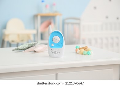 Modern baby monitor, toys and teether on table in room