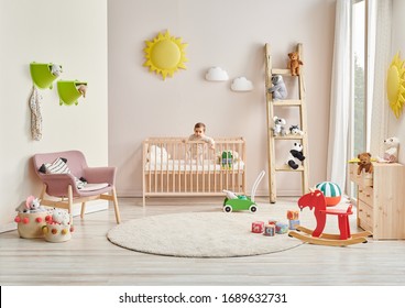 Modern baby room, wooden detail, cradle and crib, pink chair, cabinet, toy yellow sun. Baby in the bed.