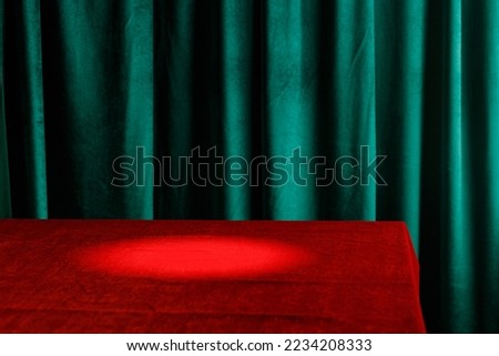 Modern background with empty red cloth table and green draped velvet curtains. Template for advertising, presentation, cosmetic products. Mockup, texture. Light spot.