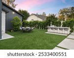 Modern backyard with artificial grass, outdoor dining set, and bar area against a sunset sky.