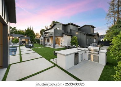 Modern backyard with outdoor kitchen, swimming pool, and lounge area at sunset. - Powered by Shutterstock