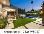 Modern backyard with a pool, patio seating, and lush greenery at dusk, showcasing outdoor living space and design.