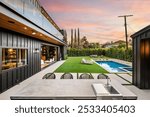 Modern backyard with a swimming pool, outdoor kitchen, and lounge area at sunset.