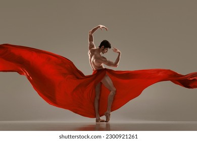 Modern ballet. Handsome young male ballet dancer performing with red silk fabric against grey studio background. Concept of art, classical dance, inspiration, creativity, fashion, beauty, choreography - Powered by Shutterstock