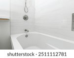 A modern bathroom featuring a sleek white bathtub against a minimalist tiled wall, emphasizing cleanliness and simplicity.