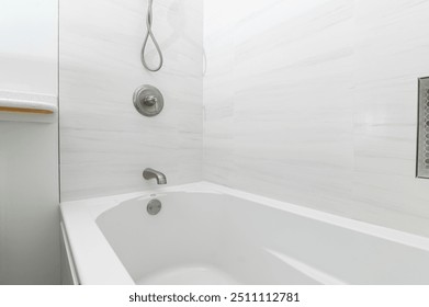 A modern bathroom featuring a sleek white bathtub against a minimalist tiled wall, emphasizing cleanliness and simplicity.