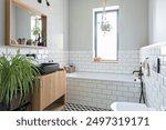 Modern bathroom in industrial design in stylish interior. White tiles, wooden cabinet and mirror and bathroom sink in black colour in new apartment.