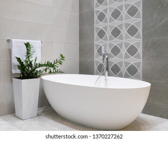modern bathroom interior design with white stone bathtub, grey tiles wall, ceramic flowerpot with green plant and hanger with towel