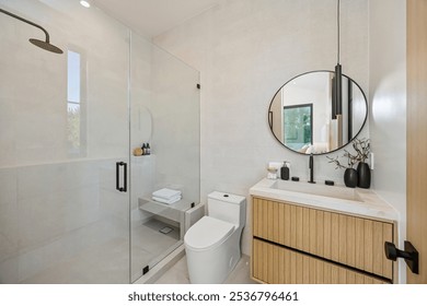 Modern bathroom interior with glass shower, wooden vanity, and round mirror, featuring minimalist decor and natural light. - Powered by Shutterstock