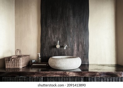 Modern bathroom interior with original white stone sink, clock, wooden baskets and soap dispenser. Wooden interior of spa in yellow and gold colors. Selective focus, only part of bathroom is in focus. - Shutterstock ID 2091413890