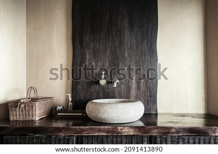 Modern bathroom interior with original white stone sink, clock, wooden baskets and soap dispenser. Wooden interior of spa in yellow and gold colors. Selective focus, only part of bathroom is in focus.